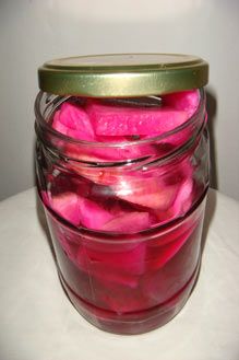 a jar filled with pink petals sitting on top of a white table next to a wall