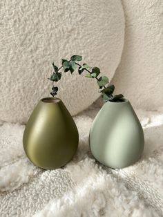 two green vases sitting next to each other on a white blanket with plants in them