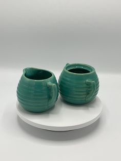 two green vases sitting on top of a white plate next to each other in front of a white background