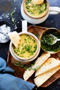 two mugs filled with soup and some pita bread on a wooden tray next to each other