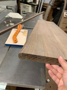 a hand holding a piece of wood in front of a table with tools on it