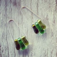 three green and black glass beads are hanging from silver earwires on a piece of wood