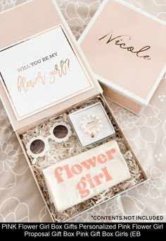 a pink flower girl gift box sits on a bed next to a card and some other items