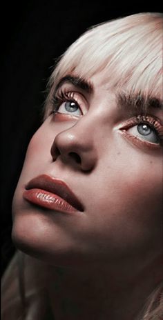 a woman with blond hair and blue eyes looks up into the sky while wearing black eyeliners