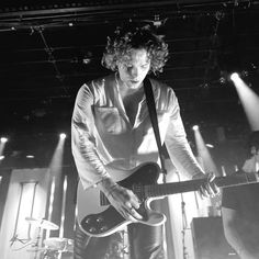 a man with curly hair playing an electric guitar in front of two other men on stage