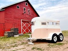 an old trailer parked in front of a red barn