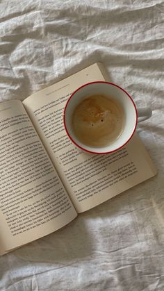 an open book with a cup of coffee sitting on top of it next to a spoon