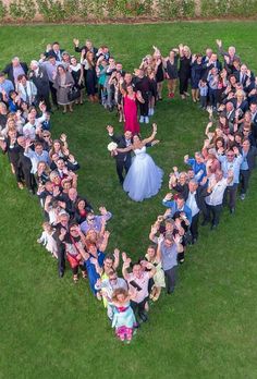 a large group of people standing in the shape of a heart on top of grass