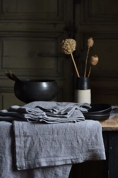 a table topped with a black bowl filled with flowers next to a gray cloth on top of a wooden table