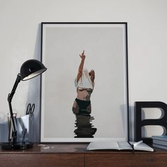 a desk with a lamp, books and a poster on it that has a woman's hand up in the air