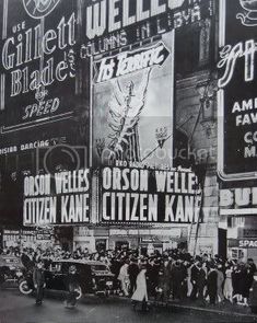 an old black and white photo of people standing in front of a building with advertisements on it