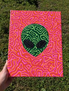 a hand holding up a piece of art that looks like an alien head with green and pink swirls on it