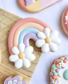 decorated cookies with flowers, hearts and rainbows on a cutting board next to them