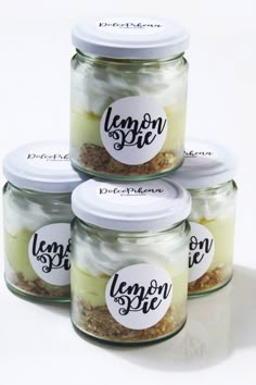 four jars with lemon pie in them sitting on a white surface, one has a label that says lemon pie