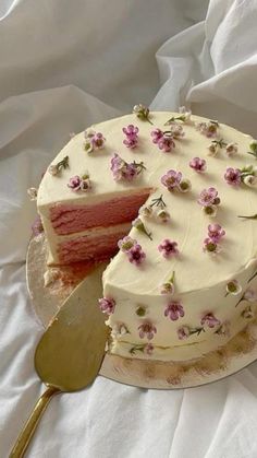 a cake with white frosting and pink flowers on it next to a slice missing from the cake