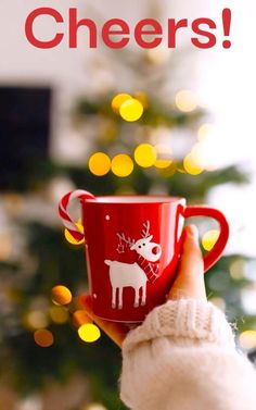 a person holding a red coffee cup in front of a christmas tree with the words cheers on it