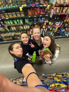 four girls standing in front of a grocery store with their arms around each other and pointing at the camera