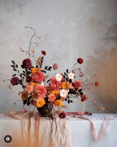 a vase filled with lots of flowers sitting on top of a white cloth covered table