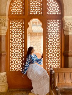 a woman in a blue and white dress leaning against a wall with an arched window