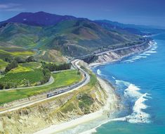 an aerial view of the ocean and coastline with a train on it's tracks