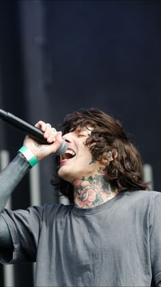 a man with long hair and piercings singing into a microphone at a music festival