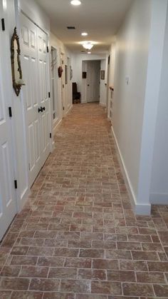 an empty hallway with white doors and brown brick flooring on both sides, leading to another room