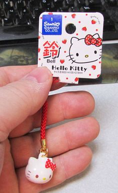 someone is holding a hello kitty keychain with a red ribbon and bow on it