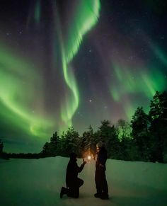 two people sitting in the snow under an aurora bore