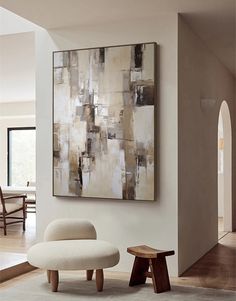 an abstract painting hangs on the wall next to a footstool in a living room