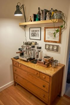 an old fashioned coffee machine on top of a wooden dresser next to a wall mounted shelf