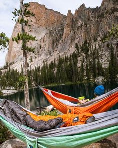 two hammocks are set up on the rocks near a body of water with mountains in the background