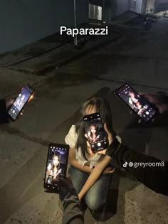 two people sitting on the ground with cell phones in their hands and one person holding them up