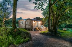 a mobile home sits in the middle of a wooded area at dusk with its lights on