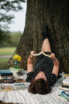 a woman laying on the ground in front of a tree with books all over her