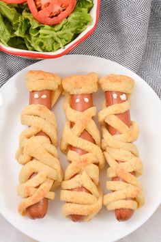 hotdogs wrapped in bread are on a plate next to a salad