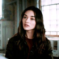 a woman with long dark hair sitting in front of a window