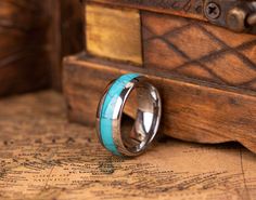 a wedding band with a turquoise inlay sits on top of a wooden box next to a map