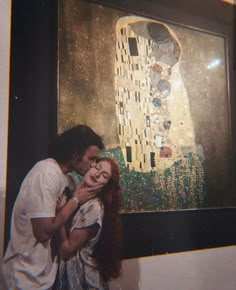 a man and woman are kissing in front of a painting that looks like the kiss