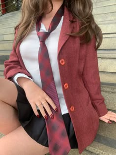 a woman wearing a red jacket and tie sitting on steps with her hands in her pockets