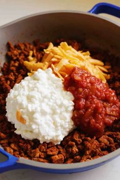 some food is in a blue pan on the table and it looks like chili, cheese, and sour cream