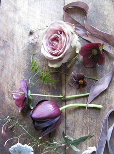 flowers and ribbons laid out on a wooden table with one pink flower in the middle