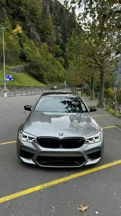 a silver car parked in a parking lot next to some trees and bushes on the side of a mountain