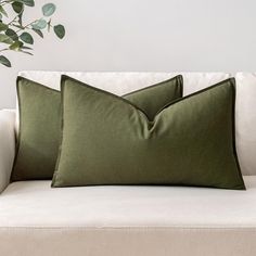 two green pillows sitting on top of a white couch next to a potted plant