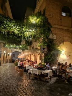 people are sitting at tables in an alleyway with greenery growing on the walls