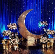 a stage with flowers and vases on the floor next to an illuminated crescent moon