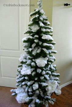 a snow covered christmas tree in the corner of a room with a white door behind it