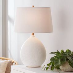 a white lamp sitting on top of a table next to a potted green plant