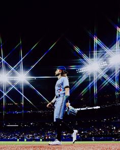 a baseball player is walking on the field at night with bright lights in the background