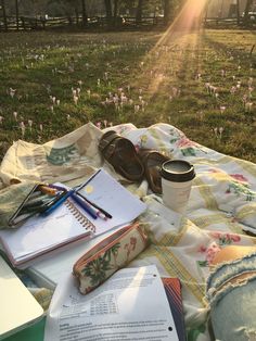 an open book, coffee cup and other items are sitting on a blanket in the grass