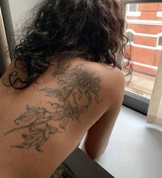 the back of a woman's body with tattoos on it, looking out a window